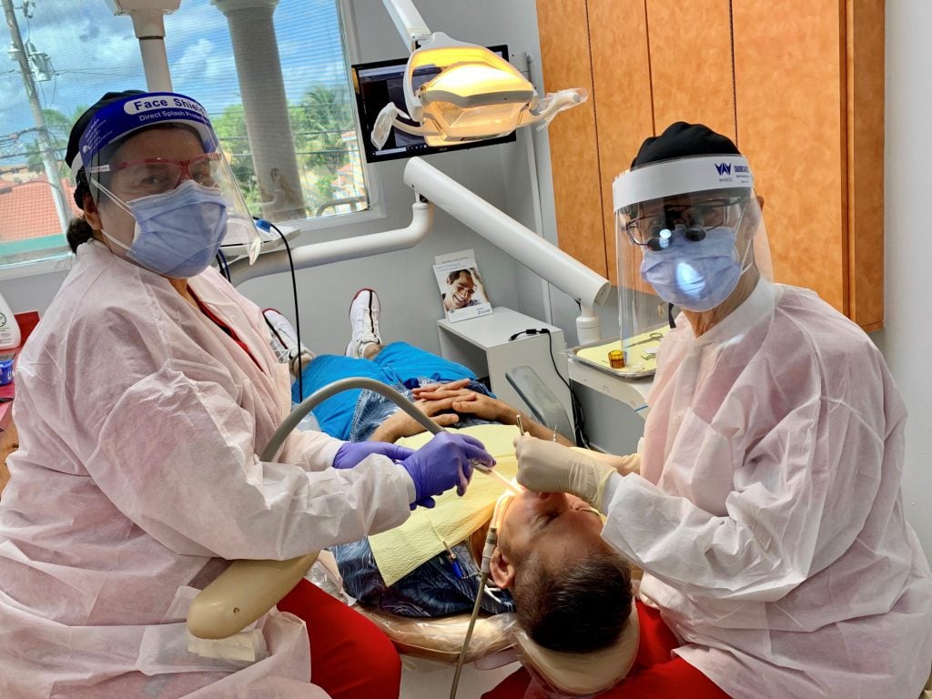 Staff with full PPE working on a patient 2 in dental chair Flagler Dental Clinic of Miami